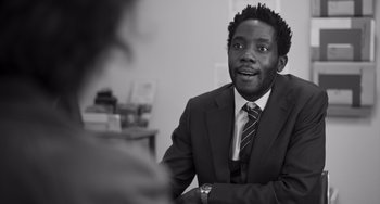 Movie still from “Paris, 13th District” (2021), directed by Jacques Audiard – A black and white photo of a man wearing a suit and tie; Close Up shot, Over the shoulder angle