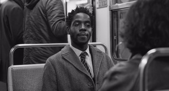 Movie still from “Paris, 13th District” (2021), directed by Jacques Audiard – A black and white photo of a man on a train; Close Up shot, Over the shoulder angle