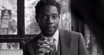 Movie still from “Paris, 13th District” (2021), directed by Jacques Audiard – A black and white photo of a man holding a glass; Close Up shot, Low angle