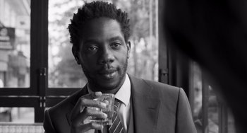 Movie still from “Paris, 13th District” (2021), directed by Jacques Audiard – A black and white photo of a man holding a glass; Close Up shot, Low angle