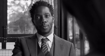 Movie still from “Paris, 13th District” (2021), directed by Jacques Audiard – A black and white photo of a man wearing a suit and tie; Close Up shot, Low angle