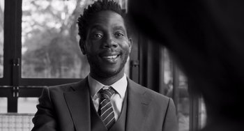 Movie still from “Paris, 13th District” (2021), directed by Jacques Audiard – A black and white photo of a man wearing a suit and tie; Close Up shot, Over the shoulder angle