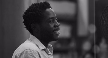 Movie still from “Paris, 13th District” (2021), directed by Jacques Audiard – A black and white photo of a man smiling; Close Up shot, Low angle