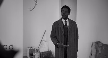 Movie still from “Paris, 13th District” (2021), directed by Jacques Audiard – A black and white photo of a man wearing a coat and tie; Medium shot, Low angle