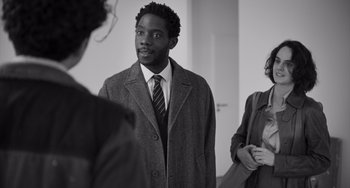 Movie still from “Paris, 13th District” (2021), directed by Jacques Audiard – A man wearing a suit and tie standing next to two women; Medium shot, Over the shoulder angle