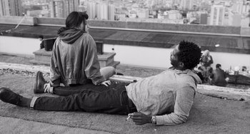 Movie still from “Paris, 13th District” (2021), directed by Jacques Audiard – A man and a woman sitting on the ground in front of a bench; Medium shot, High angle