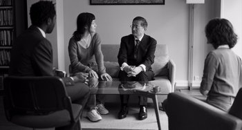 Movie still from “Paris, 13th District” (2021), directed by Jacques Audiard – A man and a woman are sitting on a couch; Medium shot, Over the shoulder angle