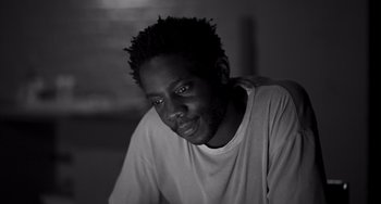 Movie still from “Paris, 13th District” (2021), directed by Jacques Audiard – A black and white photo of a man in a white shirt; Close Up shot, High angle