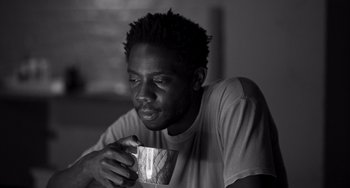 Movie still from “Paris, 13th District” (2021), directed by Jacques Audiard – A man holding a coffee cup while sitting in a room; Close Up shot, Low angle