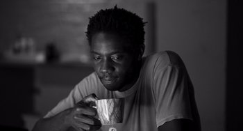 Movie still from “Paris, 13th District” (2021), directed by Jacques Audiard – A man holding a coffee cup while sitting at a table; Close Up shot, Low angle