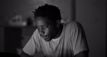 Movie still from “Paris, 13th District” (2021), directed by Jacques Audiard – A black and white photo of a man with a beard; Close Up shot, Low angle