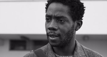 Movie still from “Paris, 13th District” (2021), directed by Jacques Audiard – A black and white photo of a man with a beard; Close Up shot, Low angle