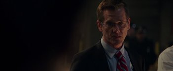 Movie still from “Patriots Day” (2016), directed by Peter Berg – A man in a suit and tie standing in front of a wall; Close Up shot, Over the shoulder angle