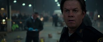 Movie still from “Patriots Day” (2016), directed by Peter Berg – A man in a black jacket is in a dark room; Close Up shot, Over the shoulder angle