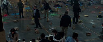 Movie still from “Patriots Day” (2016), directed by Peter Berg – A group of people standing around a room with bags on the ground; Extreme Wide shot, High angle
