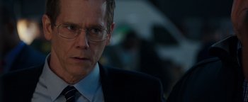 Movie still from “Patriots Day” (2016), directed by Peter Berg – A person wearing a suit and glasses; Close Up shot, Over the shoulder angle