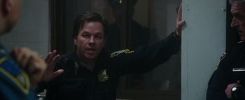 Movie still from “Patriots Day” (2016), directed by Peter Berg – A man wearing a police uniform is waving; Close Up shot, Over the shoulder angle