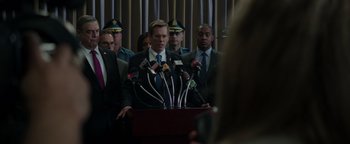Movie still from “Patriots Day” (2016), directed by Peter Berg – A group of men standing around a podium with microphones; Medium shot, Over the shoulder angle