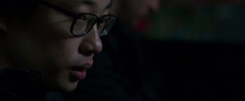 Movie still from “Patriots Day” (2016), directed by Peter Berg – A person wearing glasses looking down at something in the dark; Close Up shot, Low angle