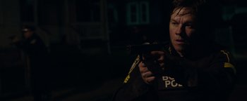 Movie still from “Patriots Day” (2016), directed by Peter Berg – A person holding a gun in a dark room; Medium shot, Over the shoulder angle