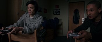 Movie still from “Patriots Day” (2016), directed by Peter Berg – A man sitting in a chair in front of a person playing a video game; Medium shot, High angle