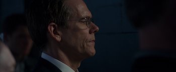 Movie still from “Patriots Day” (2016), directed by Peter Berg – A person wearing a suit and glasses; Close Up shot, Over the shoulder angle