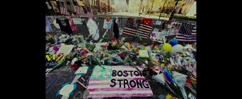 Movie still from “Patriots Day” (2016), directed by Peter Berg – A bunch of flowers that are on the ground in front of a building; Wide shot, Overhead angle