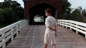 Movie still from “The Bridges of Madison County” (1995), directed by Clint Eastwood – A woman in a white dress standing on a wooden bridge; Wide shot, Over the shoulder angle