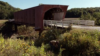 Movie still from “The Bridges of Madison County” (1995), directed by Clint Eastwood – A person in a field near a covered bridge; Extreme Wide shot, Over the shoulder angle