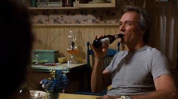 Movie still from “The Bridges of Madison County” (1995), directed by Clint Eastwood – A man sitting at a table drinking a beer; Medium shot, Over the shoulder angle