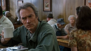 Movie still from “The Bridges of Madison County” (1995), directed by Clint Eastwood – A man sitting at a table in front of other people; Close Up shot, Over the shoulder angle