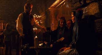 Movie still from “The Brothers Grimm” (2005), directed by Terry Gilliam – A group of people sitting around a table with lit candles; Medium shot, Over the shoulder angle