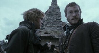 Movie still from “The Brothers Grimm” (2005), directed by Terry Gilliam – Two men standing next to each other in front of a stone building; Medium shot, Low angle
