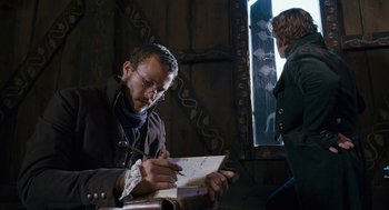 Movie still from “The Brothers Grimm” (2005), directed by Terry Gilliam – A man writing on a piece of paper in front of a woman; Medium shot, Over the shoulder angle