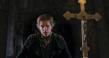 Movie still from “The Brothers Grimm” (2005), directed by Terry Gilliam – A man standing in front of a wooden cross; Medium shot, Low angle