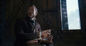 Movie still from “The Brothers Grimm” (2005), directed by Terry Gilliam – A man sitting in front of a window holding a book; Medium shot, Low angle