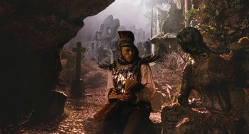 Movie still from “The Brothers Grimm” (2005), directed by Terry Gilliam – A man dressed in medieval clothing sitting in a cave; Wide shot, Low angle