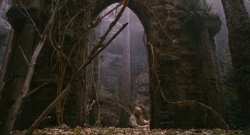 Movie still from “The Brothers Grimm” (2005), directed by Terry Gilliam – A man sitting in front of an archway in a forest; Wide shot, Low angle
