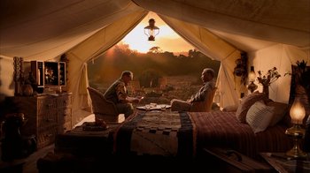 Two men sitting in front of an open tent with a sunset in the background