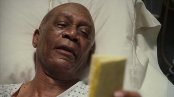 Movie still from “The Bucket List” (2007), directed by Rob Reiner – An older man laying in a hospital bed reading a book; Close Up shot, Overhead angle