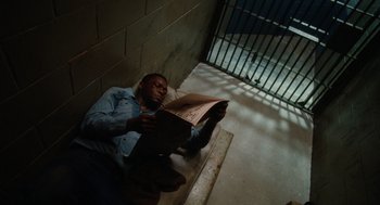Movie still from “The Butler” (2013), directed by Lee Daniels – A man sitting on the ground reading a newspaper; Medium shot, High angle