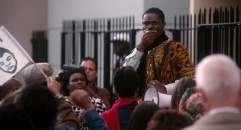 Movie still from “The Butler” (2013), directed by Lee Daniels – A group of people gathered around a man in an orange and black outfit; Medium shot, Over the shoulder angle