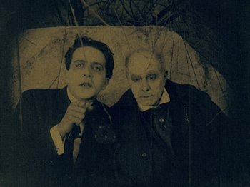 Movie still from “The Cabinet of Dr. Caligari” (1920), directed by Robert Wiene – Two men are standing under an open umbrella; Medium shot, Low angle