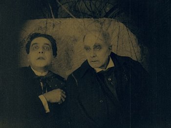Movie still from “The Cabinet of Dr. Caligari” (1920), directed by Robert Wiene – A man and a woman standing next to each other under an umbrella; Medium shot, High angle