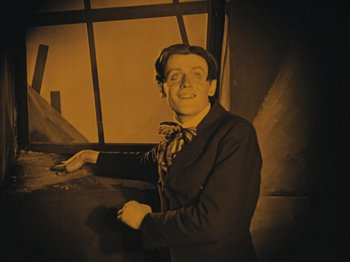 Movie still from “The Cabinet of Dr. Caligari” (1920), directed by Robert Wiene – A man wearing a suit and tie smiling for the camera; Medium shot, Low angle