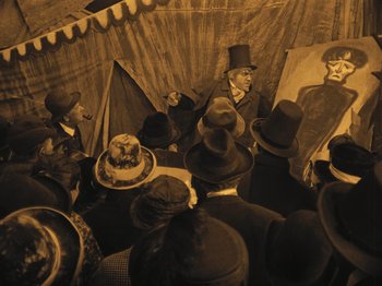Movie still from “The Cabinet of Dr. Caligari” (1920), directed by Robert Wiene – A group of people wearing hats and standing in front of a painting; Wide shot, Low angle