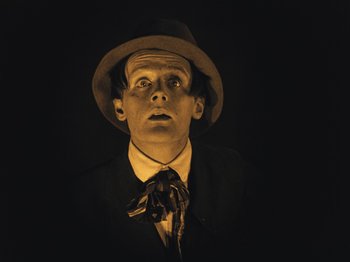 Movie still from “The Cabinet of Dr. Caligari” (1920), directed by Robert Wiene – A man wearing a suit and tie and a hat; Close Up shot, Low angle