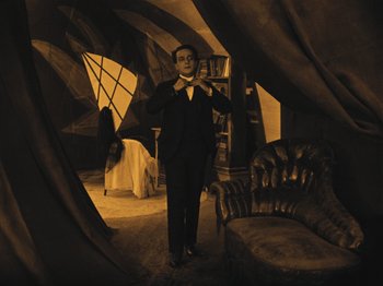 Movie still from “The Cabinet of Dr. Caligari” (1920), directed by Robert Wiene – A man in a suit and tie holding an umbrella in a room; Wide shot, High angle