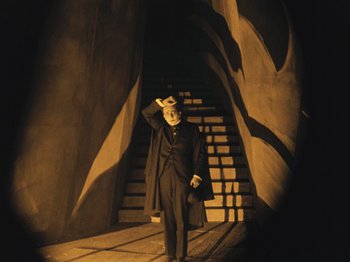 Movie still from “The Cabinet of Dr. Caligari” (1920), directed by Robert Wiene – A man standing in front of stairs in a dark room; Wide shot, Low angle