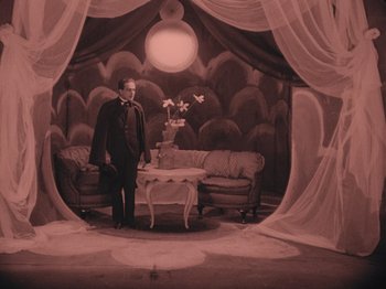 Movie still from “The Cabinet of Dr. Caligari” (1920), directed by Robert Wiene – A man standing in front of a living room with curtains; Wide shot, High angle